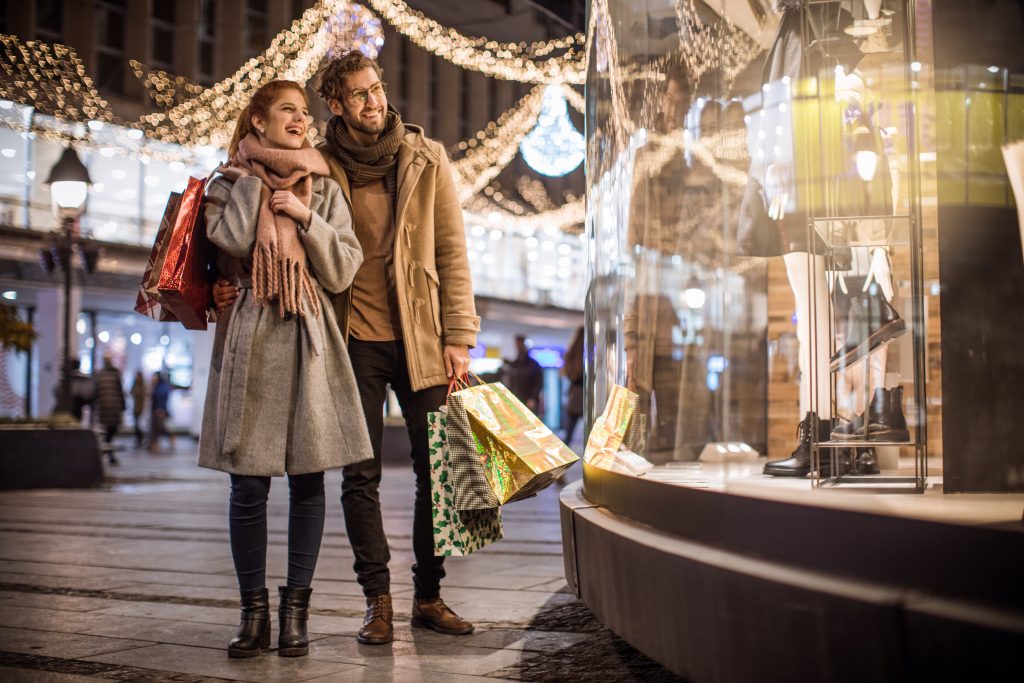 Young couple walking in shopping mall for Christmas. Holding Christmas gifts and wearing warm clothing.